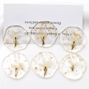 Macro detail of oval clear resin charms with real white dried flowers and gold foil flakes