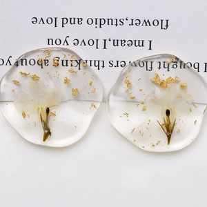 Macro shot of oval resin charms with embedded real white flowers and gold foil flakes
