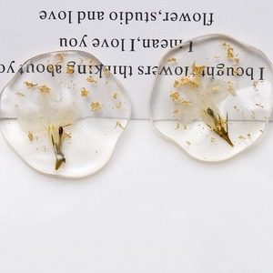Detail of oval resin charm with dried white flowers and gold foil flakes for DIY jewelry