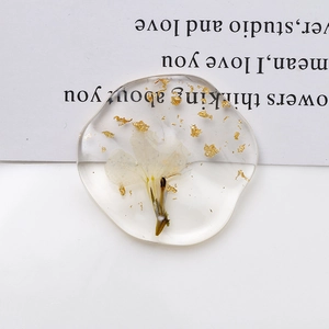 Macro detail of clear oval resin pendant featuring white dried flowers and gold foil flakes
