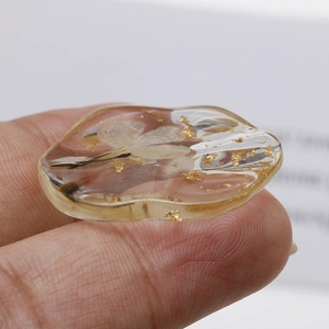 Macro view of transparent resin pendant with dried flower petals and gold foil flakes