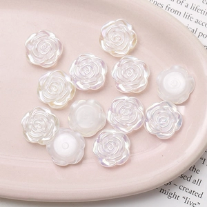 Macro shot of iridescent aurora resin camellia flower charms on a pink tray for DIY jewelry