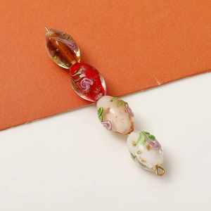 Close-up of four colorful oval glass beads with gold foil and flower leaf patterns