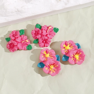 Macro detail of glossy pink resin flower charms with yellow stamen and green leaves