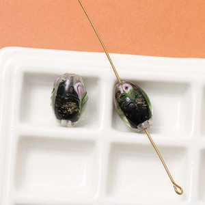 Macro shot of oval black glass bead with lavender flowers, green leaves and gold foil