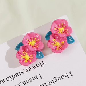 Macro detail of pink flower earrings with yellow centers and blue leaves on card