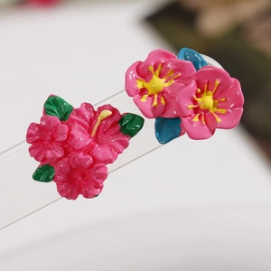 Macro shot of pink resin flower earrings with yellow centers and green leaves on a clear stand