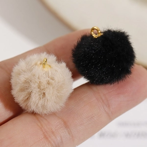 Close-up of 20mm soft plush pom poms in black and beige with gold metal loops for DIY jewelry