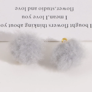 Close-up of soft grey plush pom-pom charms with gold metal rings for DIY jewelry