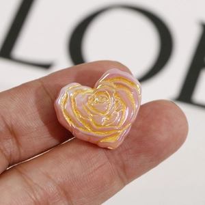 Macro shot of heart-shaped pearlescent beads with golden rose patterns for DIY jewelry