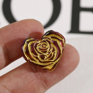 Macro shot of heart-shaped iridescent bead with gold rose relief for DIY jewelry