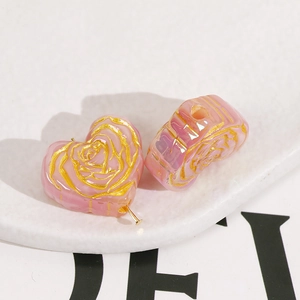 Macro shot of heart-shaped pink resin beads with golden rose patterns and center hole