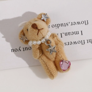 Close-up of plush bear accessory with pearl necklace, metal star and pink heart gem