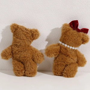 Detailed view of plush brown teddy bears with red velvet bows and pearl necklace charms