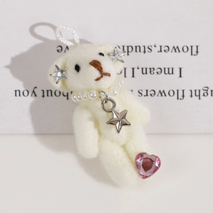 Close-up of white plush bear keychain with pearl necklace and silver star earring