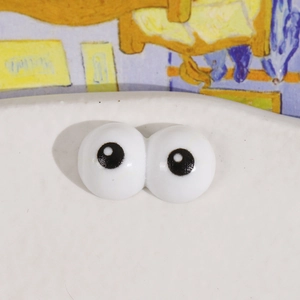 Detail of white resin cartoon big eyes charm for DIY crafts on artistic background