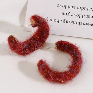 Close-up of red plush wool wrapped C-shape earrings with colorful metallic silk detail