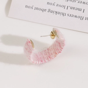 Macro view of C-shaped pink and white fuzzy yarn wrapped earring with golden stud pin