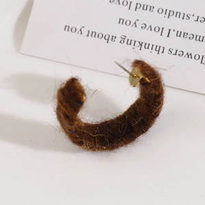 Close-up of a C-shaped earring with dark brown wool yarn wrap and golden metal studs