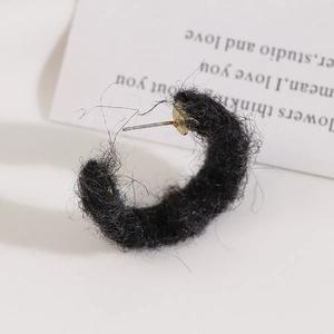 Detail view of C-shaped earrings wrapped in black plush wool with gold metal pins