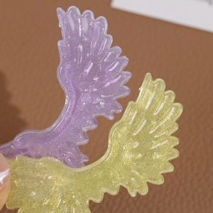Macro detail of gradient glitter angel wing resin charms in purple and yellow hues