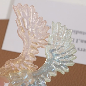 Macro shot of translucent resin angel wing charms with colorful glitter and detailed texture