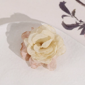 Detailed close-up of handmade cream and pink fabric rose hair clip on a white ceramic plate