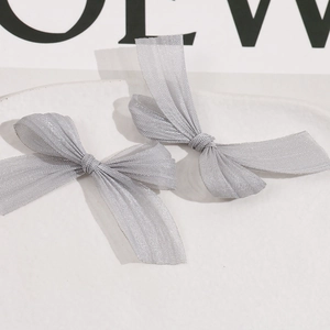 Detail of grey mesh bow hair clips with metallic luster on white ceramic tray