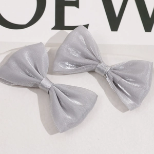Detalle de dos pinzas para el cabello con lazo brillante gris plata sobre fondo claro