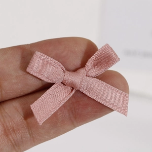 Gros plan d'un petit nœud en ruban de satin rose avec texture tissée pour bijoux DIY