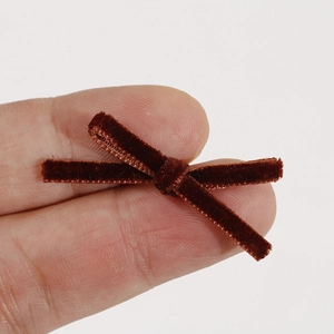 Close-up of a tiny dark brown velvet bow held between fingers for DIY hair accessories