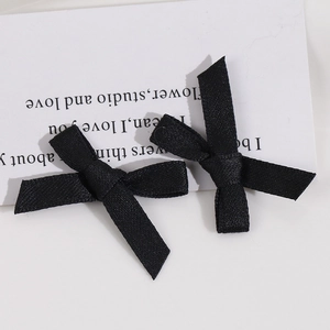 Détail de deux barrettes à nœuds en tissu noir fait main sur une carte décorative blanche