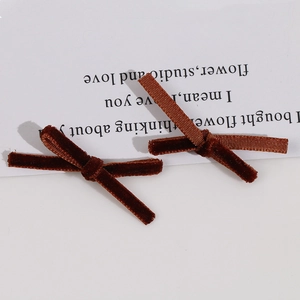 Detail view of two brown velvet bow hair clips on a minimalist white card background