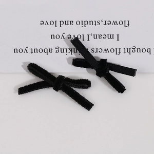 Macro detail of two black velvet handmade bow hair clips on a minimalist beige background