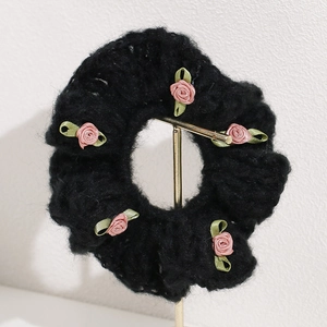 Close-up of black plush scrunchie with five handmade pink ribbon roses and green leaves