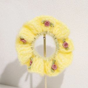 Detail of yellow knit hair scrunchie featuring five pink ribbon roses and green leaves