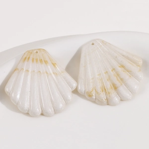 Pendentifs en résine nacre forme coquille avec texture marbrée sur plateau céramique