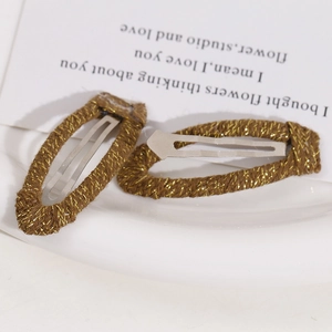 Macro view of teardrop snap hair clips with brown and gold woven metallic threads
