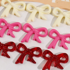 Macro detail of glossy resin bow charms for DIY jewelry in cream, pink and red tones