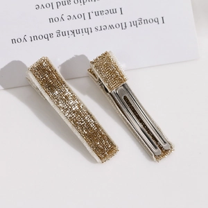 Vue détaillée de deux pinces à cheveux à paillettes dorées avec texture métallique