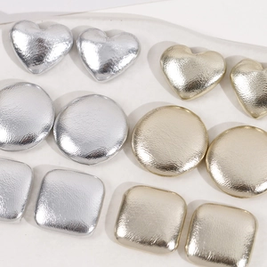 Close-up of heart, round, and square geometric metal accessories in gold and silver