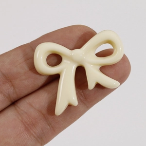 Close-up of cream-colored resin bow ornament held in hand for DIY jewelry scaling