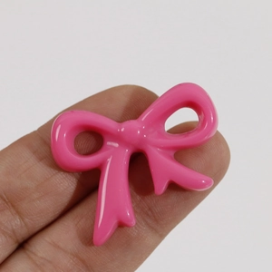 Close-up of a glossy pink resin bow accessory shown on fingertips for size reference