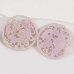 Détail macro de pendentifs en acrylique lilas avec motifs de phénix évidés et paillettes dorées