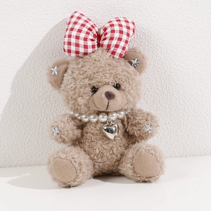 Close-up of curly plush bear with red plaid bow, pearl necklace and heart metal pendant