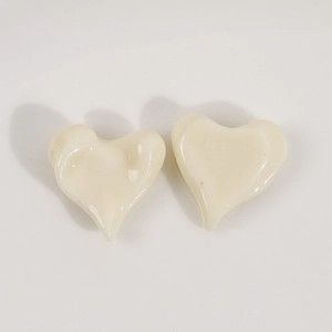 Detail of two off-white resin heart-shaped DIY accessories with glossy uneven surface
