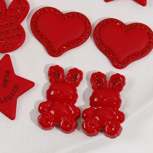 Macro detail of red glitter acrylic charms in heart and bunny shapes with small rhinestones