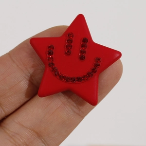 Macro detail of red star-shaped acrylic charm with rhinestone smiley face pattern