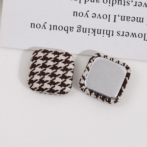 Macro detail of square houndstooth fabric buttons with smooth silver metal backing