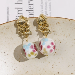 Close-up of golden irregular lava metal earrings with colorful floral glass beads